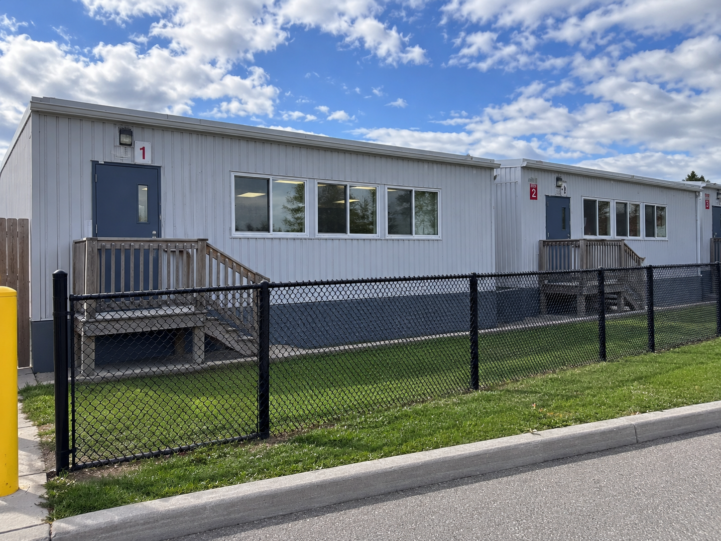 Row of portable classrooms at a school, behind a fence on a sunny day.
